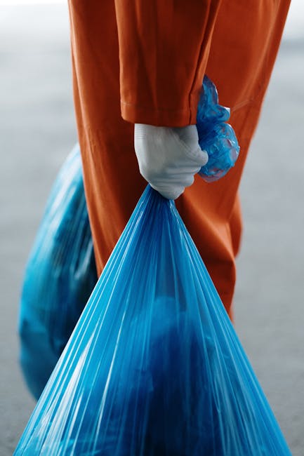 In the foreground, there is a pile of mixed waste materials placed on a paved driveway. The refuse includes several black and blue plastic garbage bags, some of which are partially torn, revealing con